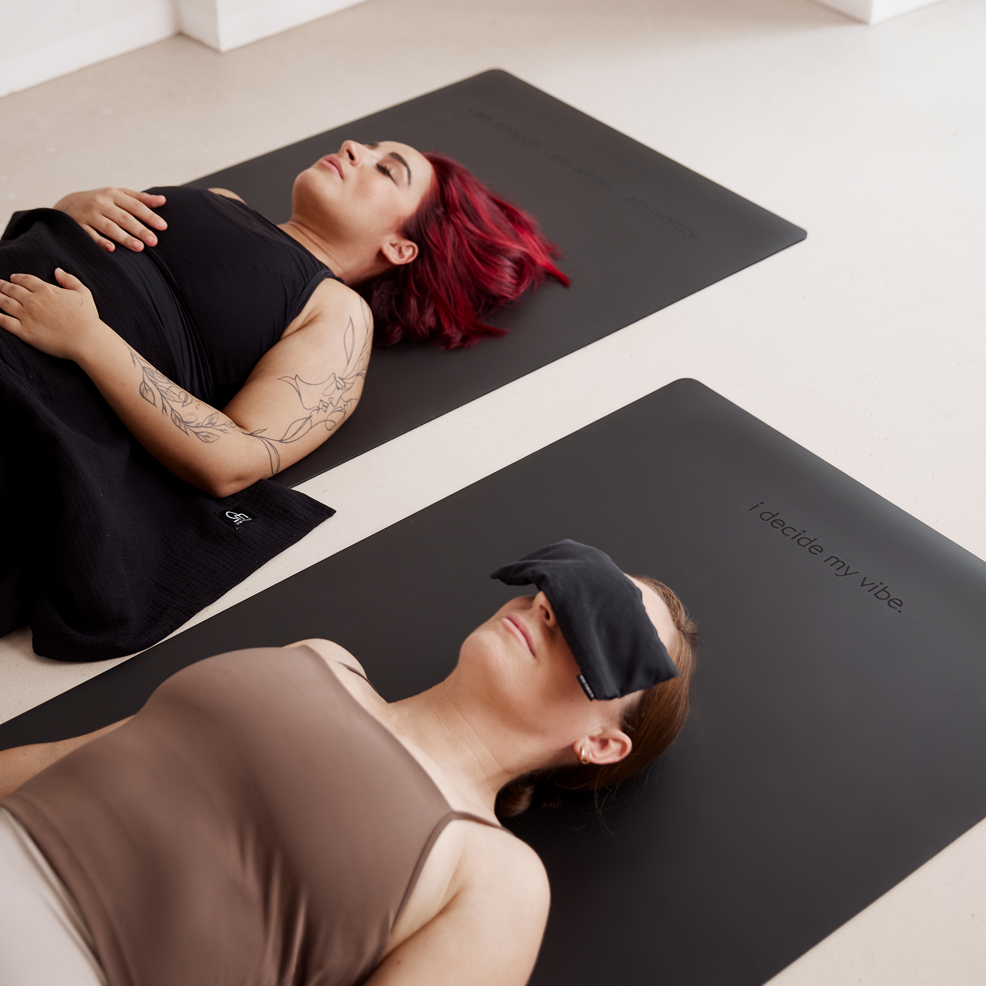 Personen mit Yogadecke und Augenkissen auf schwarzer Yogamatte