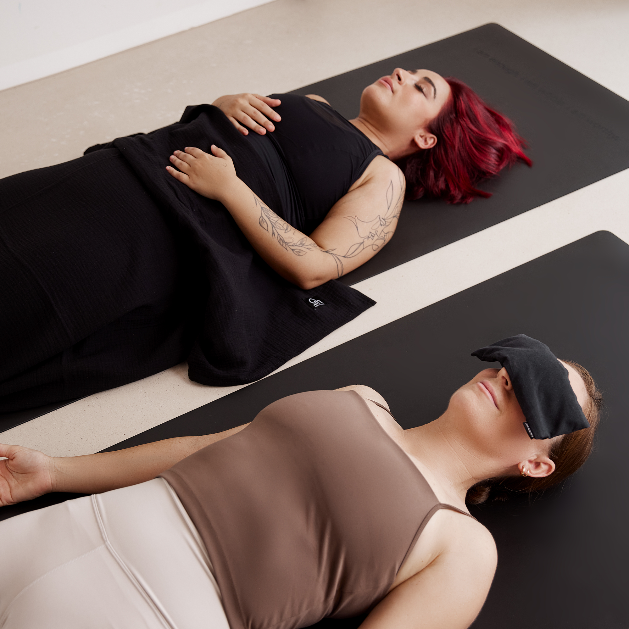 Personen mit Yogadecke und Augenkissen auf schwarzen Yogamatten